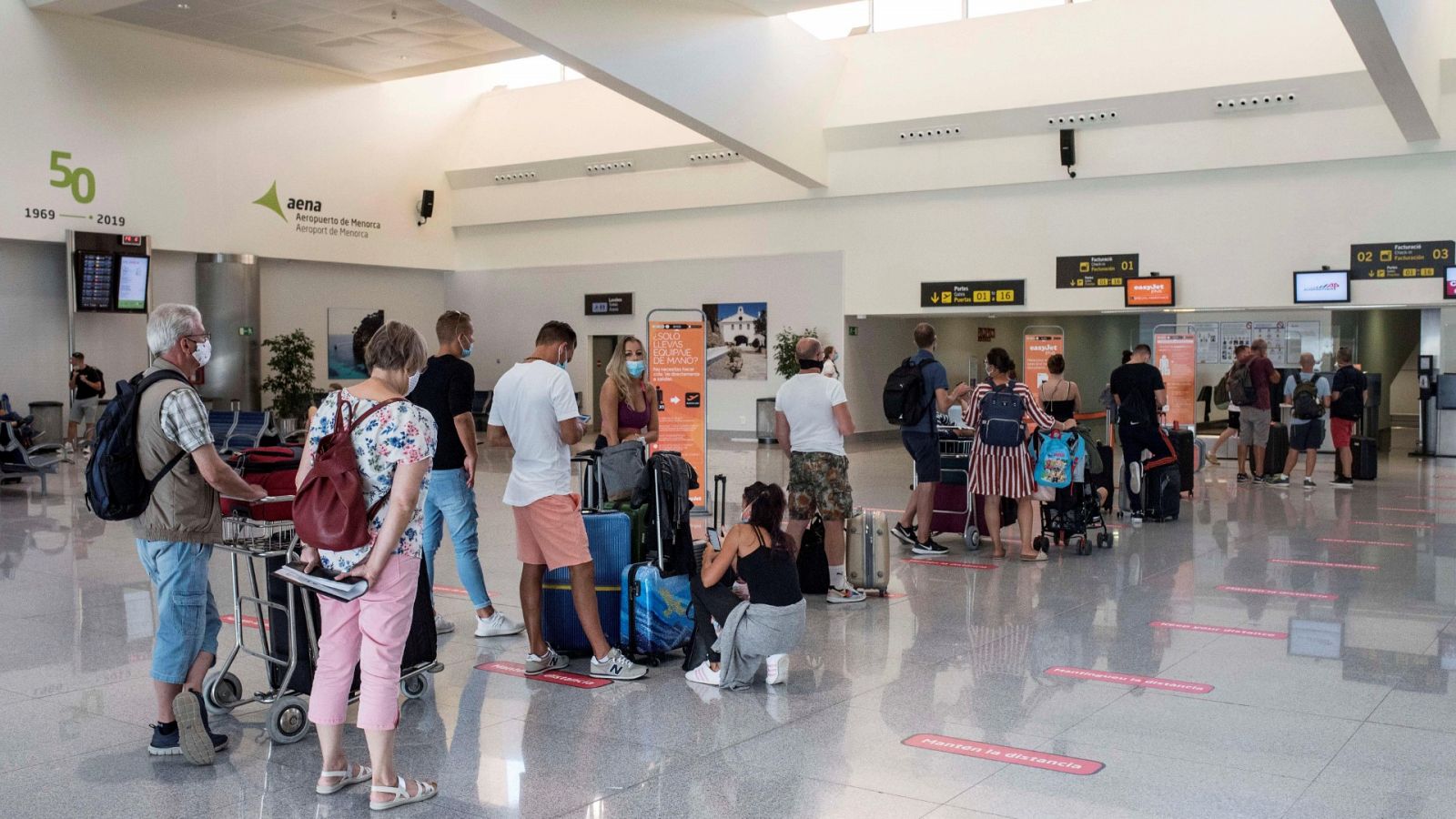Varios turistas hacen cola en uno de los mostradores del aeropuerto de Mahón (Menorca).