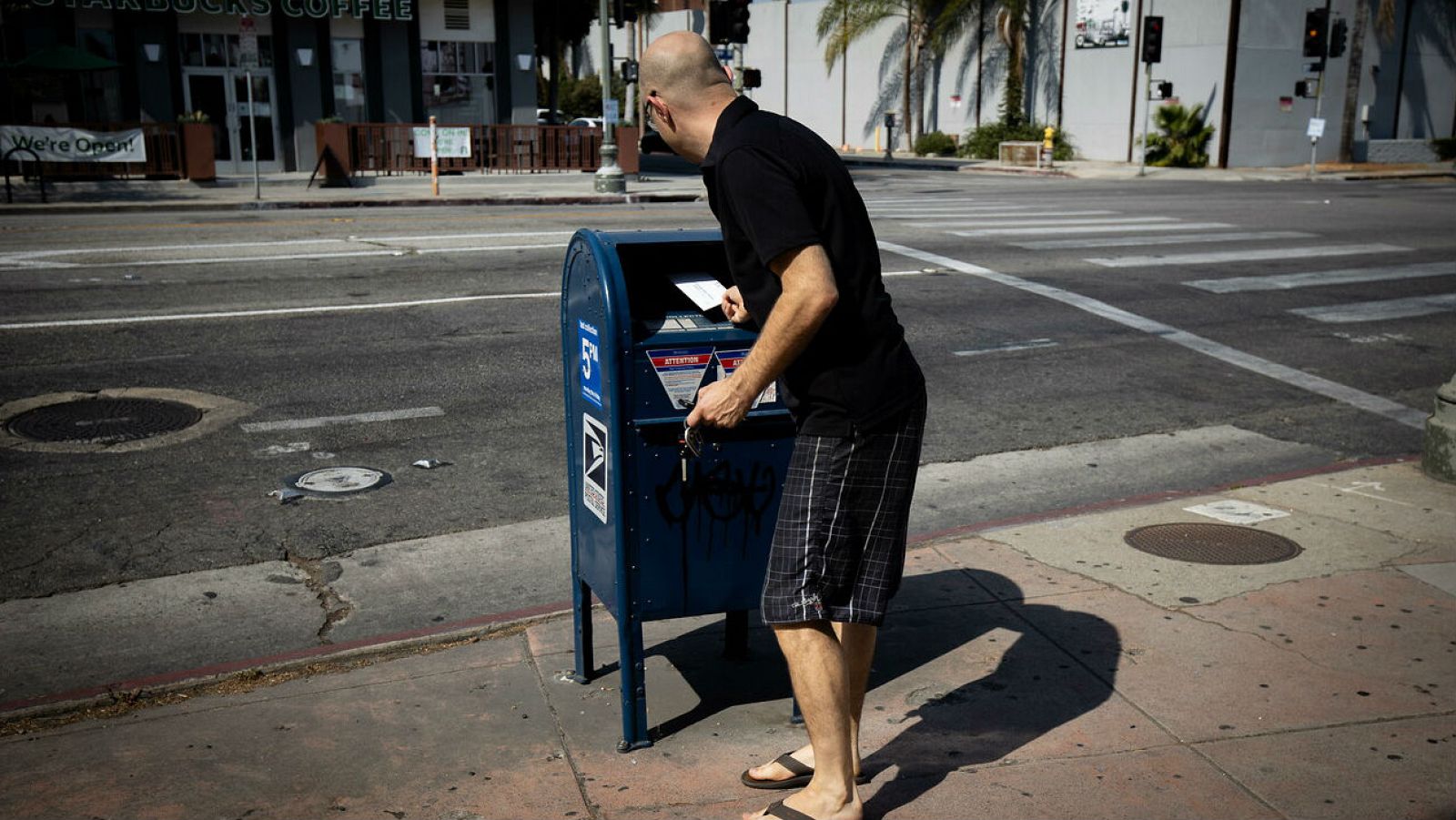 Un hombre arroja correo en un buzón de correo de USPS frente a una oficina de correos en Los Ángeles, California.
