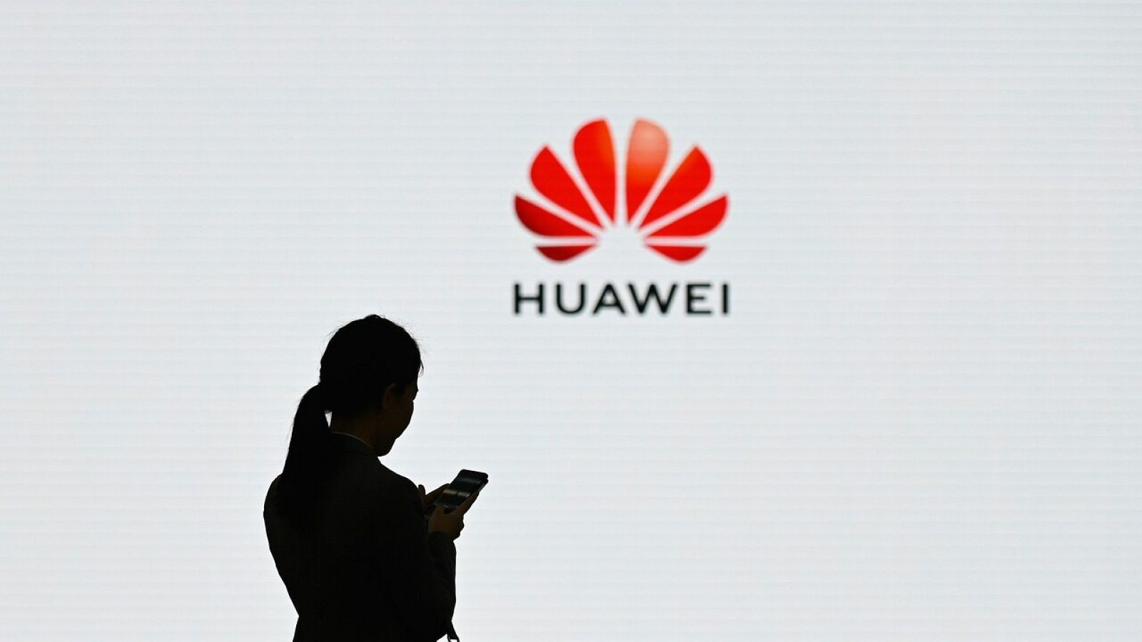 Una mujer utiliza su teléfono móvil frente al logo de Huawei