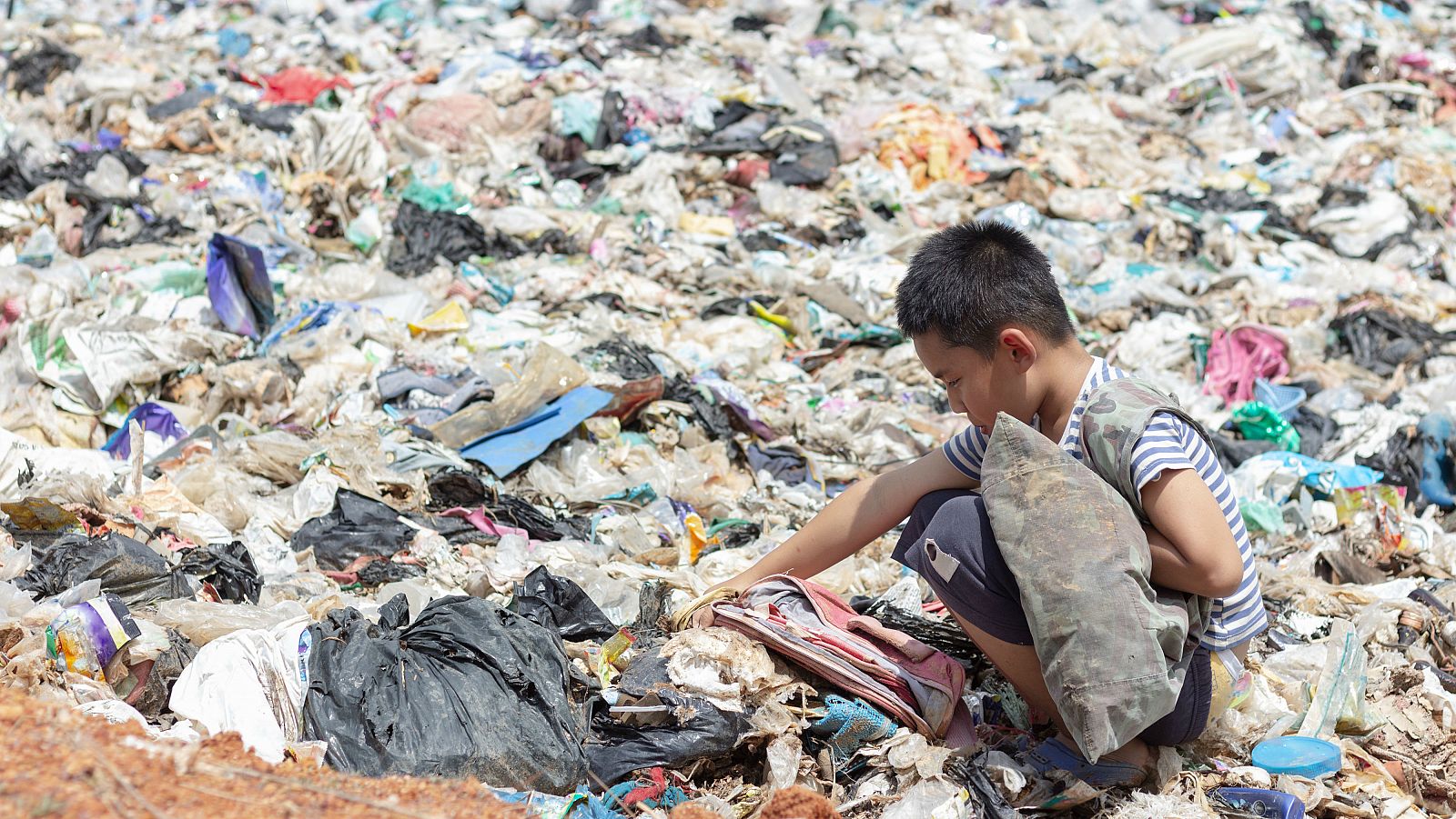 Un niño recogiendo basura en su saco para ganarse la vida.