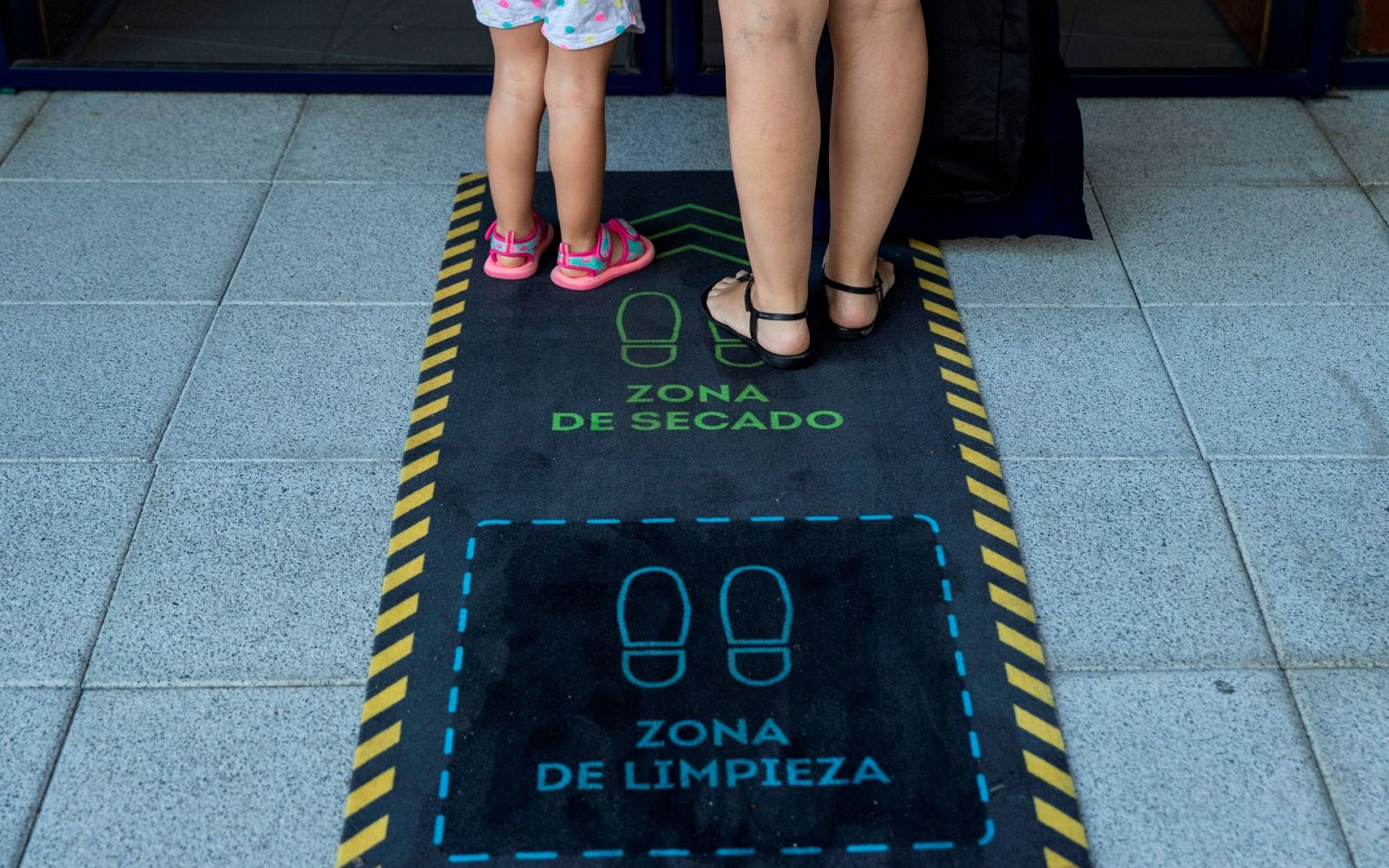 Una madre y su hija se limpian los zapatos en la puerta de una escuela infantil en Madrid