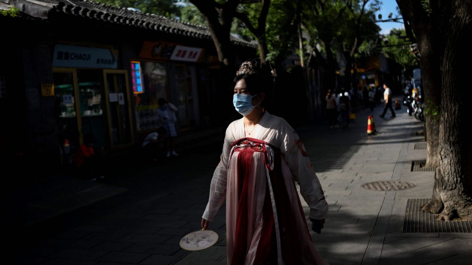 Una mujer con mascarilla y con un traje tradicional chino caminando por una calle de Pekín.