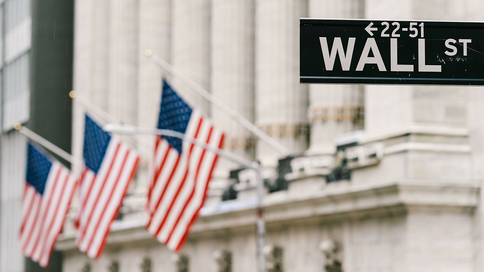 Cartel de Wall Street con banderas nacionales estadounidenses en segundo plano en el distrito financiero de la ciudad de Nueva York, en EE.UU.