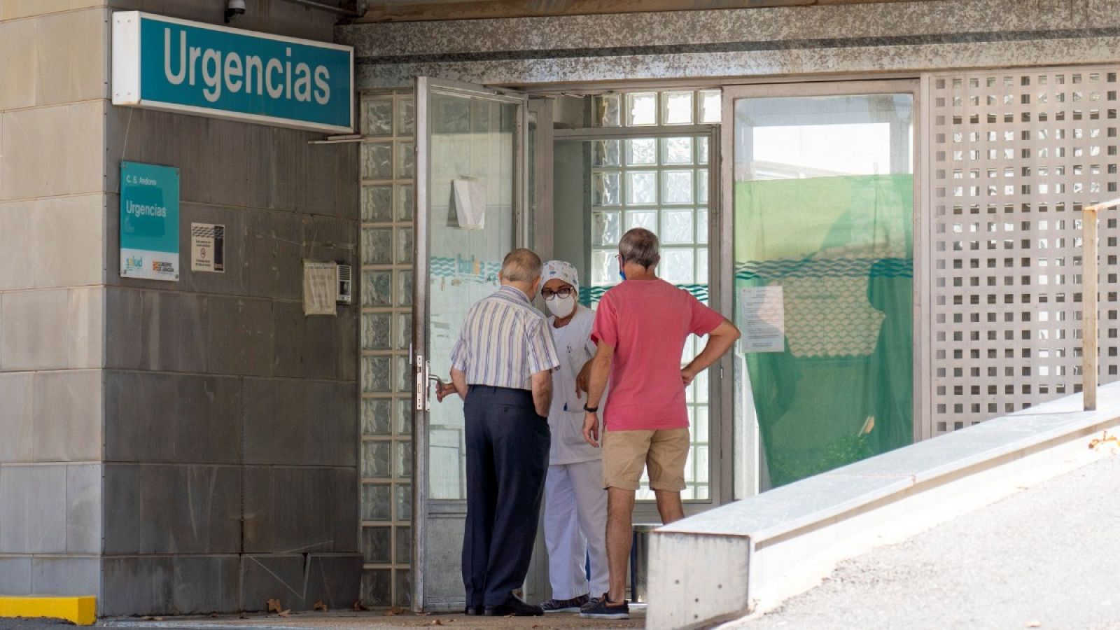 Una trabajadora del centro de salud de Andorra (Teruel) habla con dos vecinos que se acercan a la puerta de Urgencias