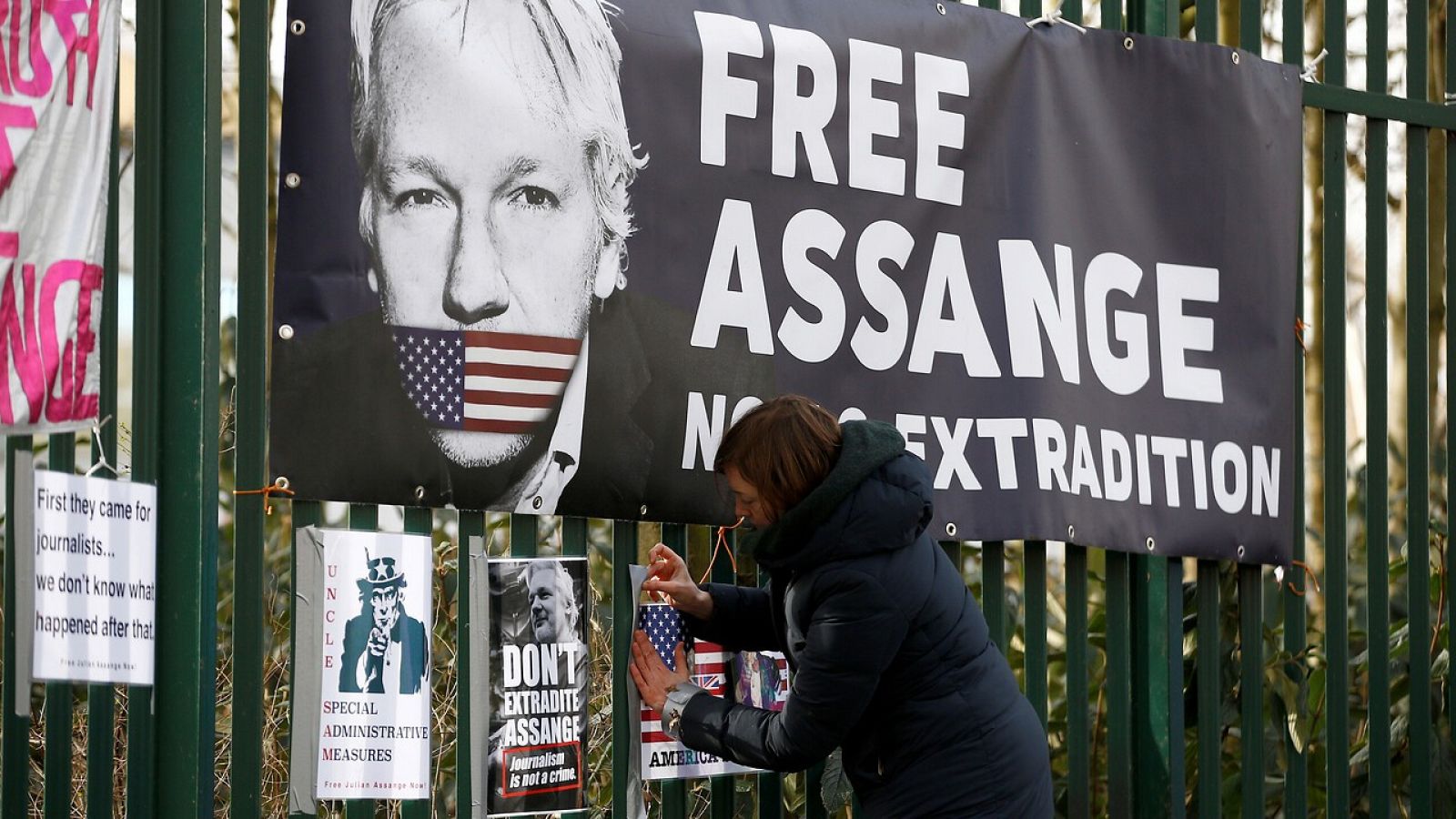 Una mujer pone  un cartel en la valla de Woolwich Crown Court en favor de Assange