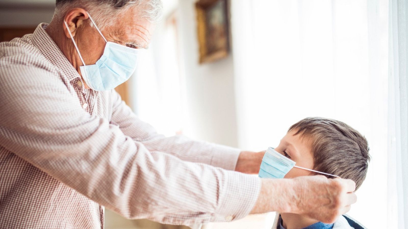 Un abuelo coloca la mascarilla a su nieto