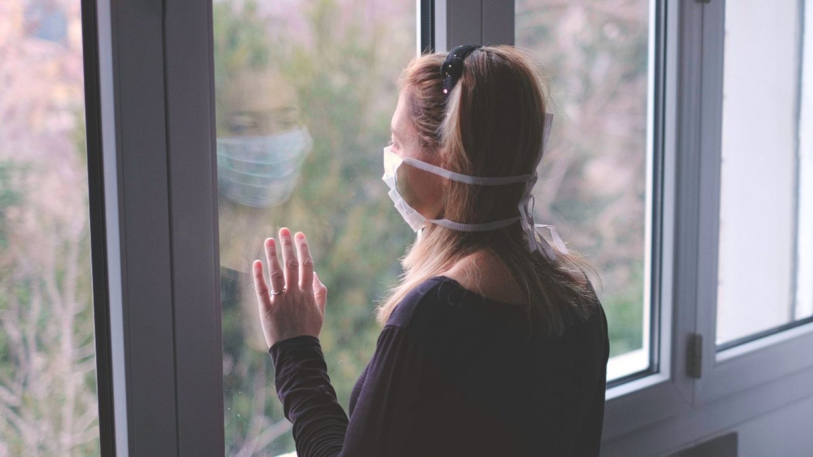 Una paciente con mascarilla mira por la ventana