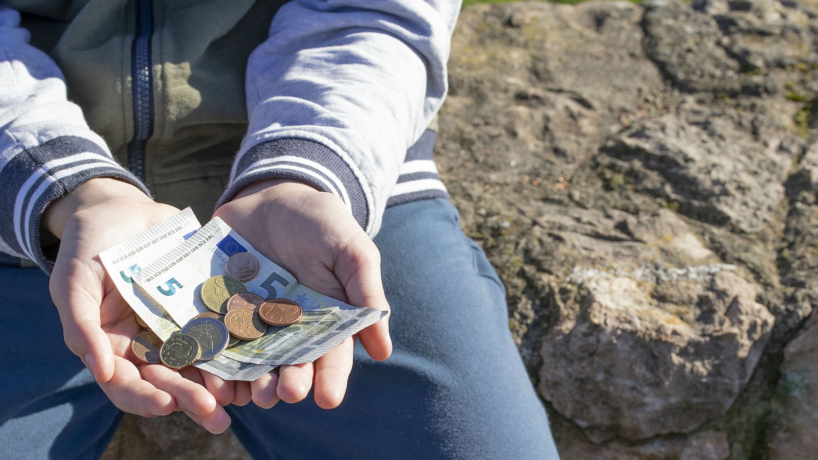 Un niño sostiene monedas y billetes de euro en sus manos.