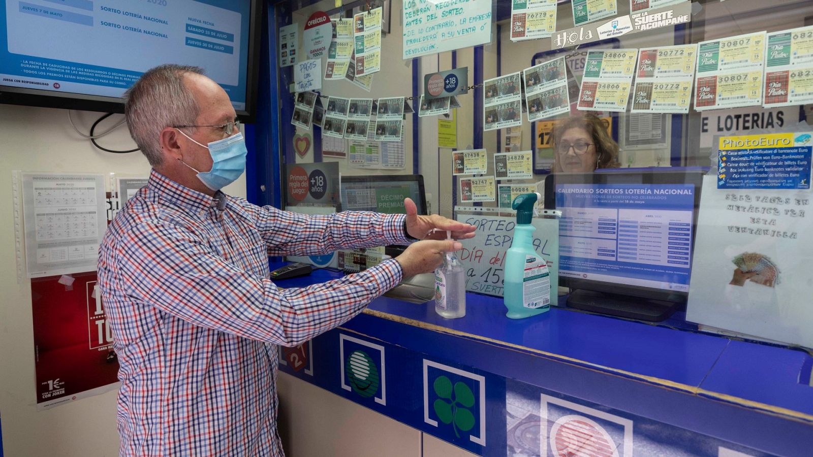 Un hombre se lava las manos con gel hidroalchólico antes de comprar lotería en una foto de archivo