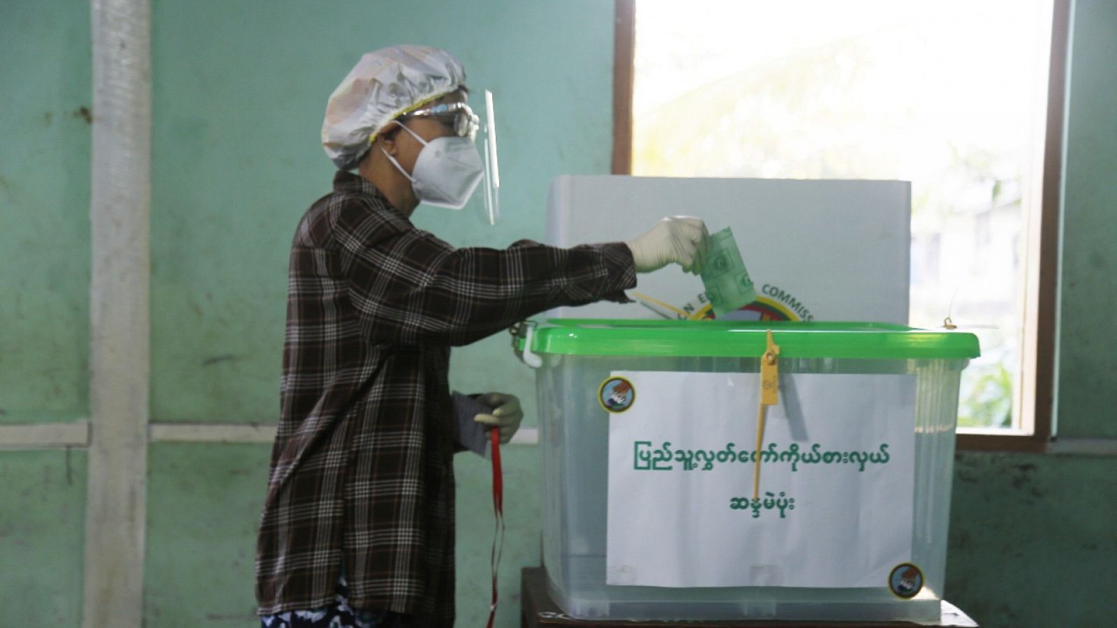 Una persona con mascarilla y máscara protectora depositando su voto en un colegio electoral en  Sittwe, Myanmar (Birmania).