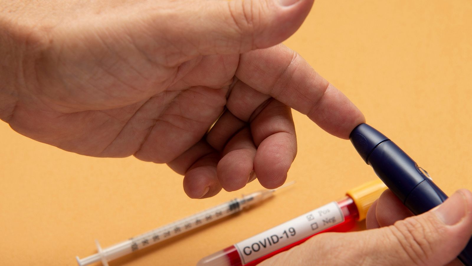 Una persona haciéndose la prueba de glucosa en sangre en la yema del dedo junto a un tubo para análisis con una etiqueta de COVID-19.