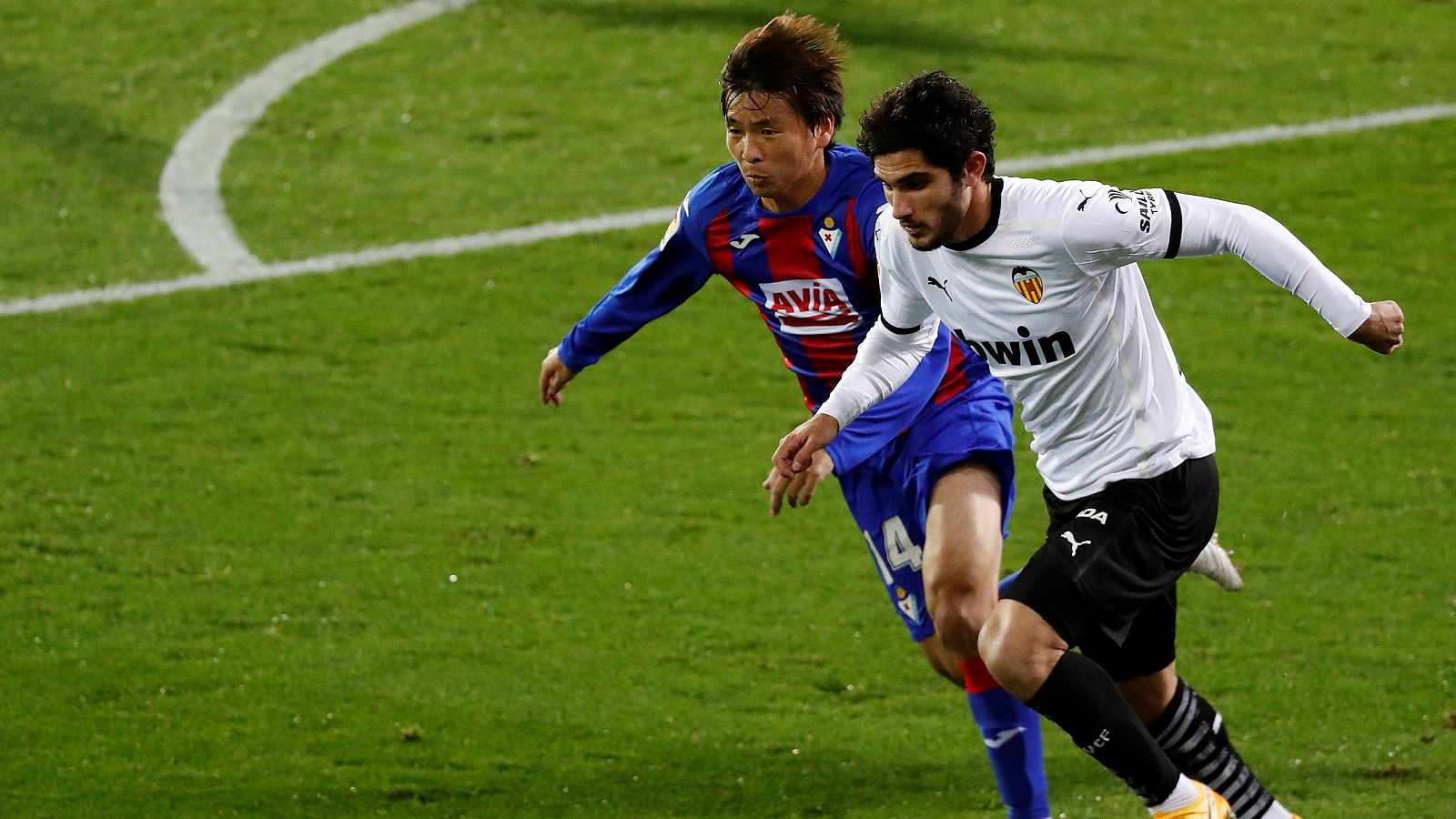 El centrocampista portugués del Valencia CF Gonçalo Guedes (d) persigue el balón con el japonés Takashi Inui, de la SD Eibar