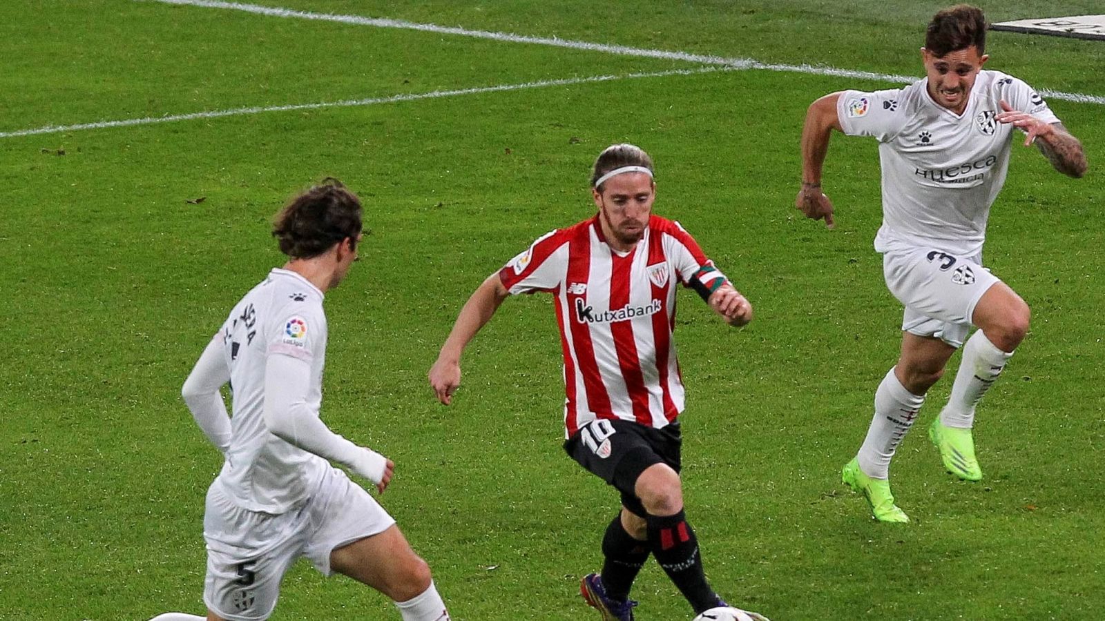 El centrocampista del Athletic Iker Muniain (c) juega un balón entre Pablo Maffeo (d) y Pedro Mosquera, ambos del Huesca.