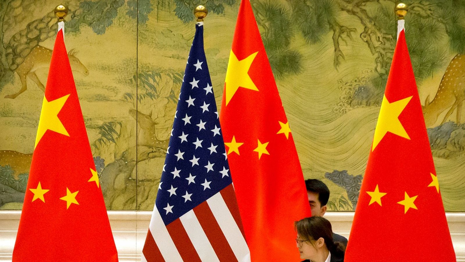 Una persona ajustando una bandera estadounidense entre tres banderas chinas antes de la sesión de apertura de las negociaciones comerciales entre China y Estados Unidos en Pekín, el 14 de febrero de 2019.