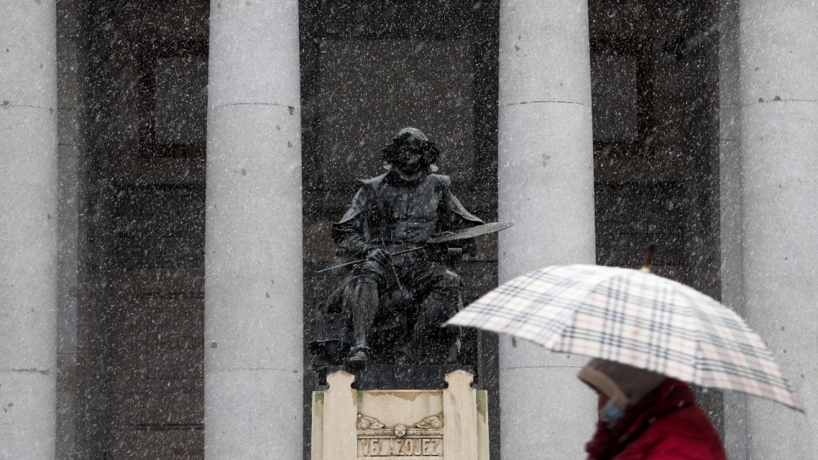 Una mujer caminando bajo la nieve frente a la estatua de Velázquez en el exterior del Museo del Prado de Madrid.