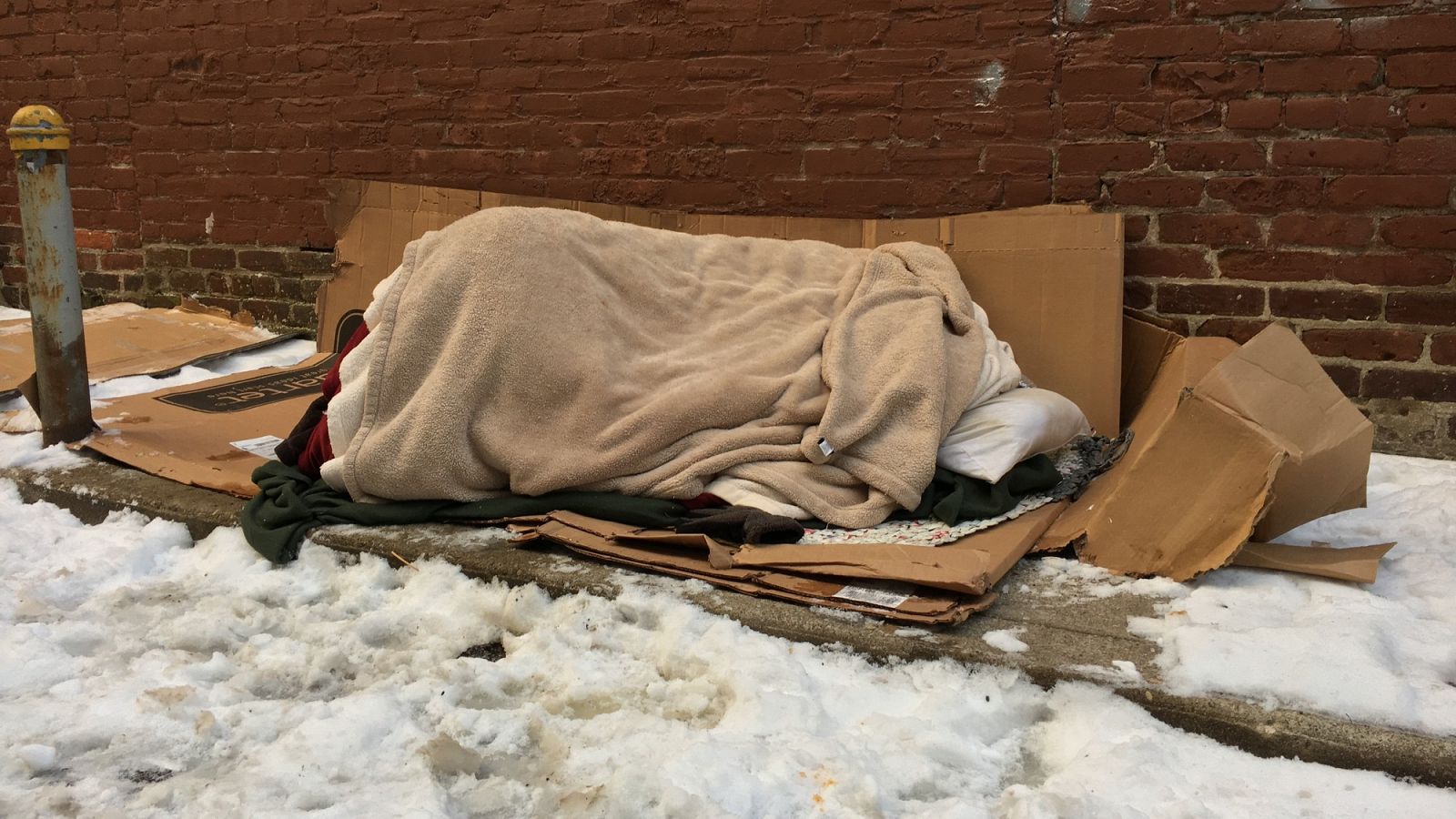 Una persona sin hogar durmiendo en la calle rodeada de nieve.