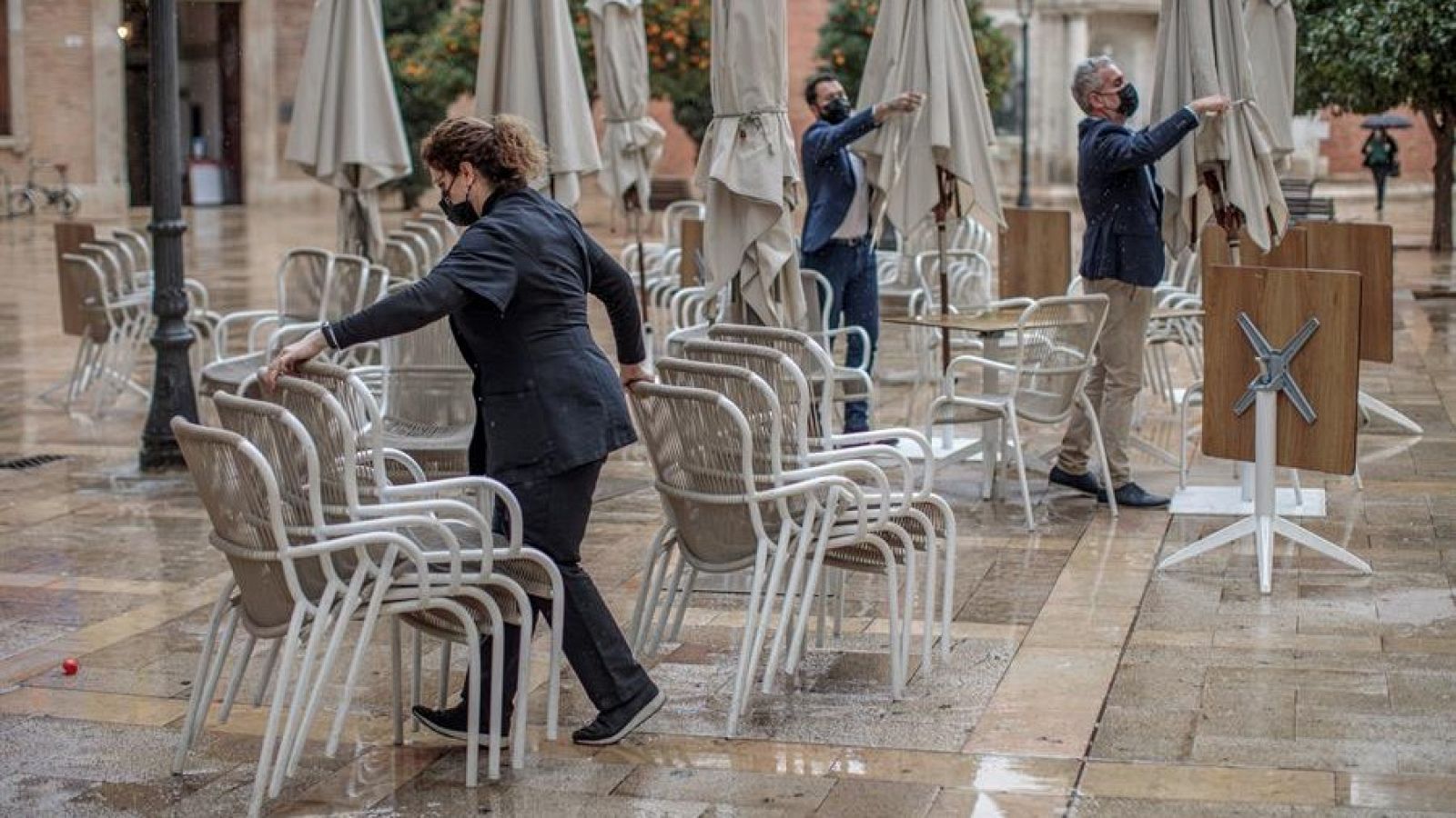 Trabajadores de un restaurante del centro de Valencia recogen las mesas y sillas de la terraza.