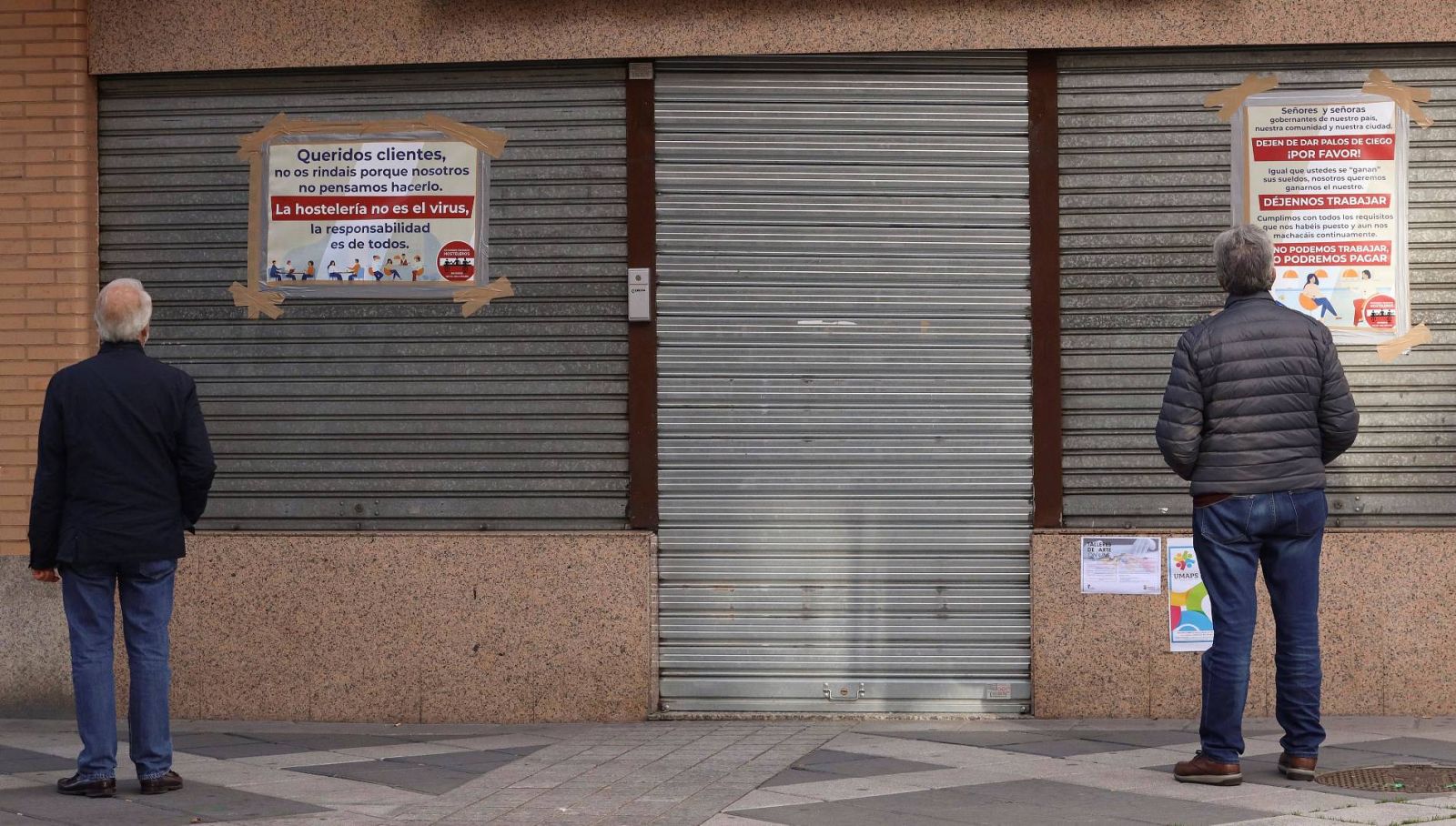 Vecinos leen los carteles de protesta colocados por un hostelero a las puertas de su negocio cerrado en Salamanca