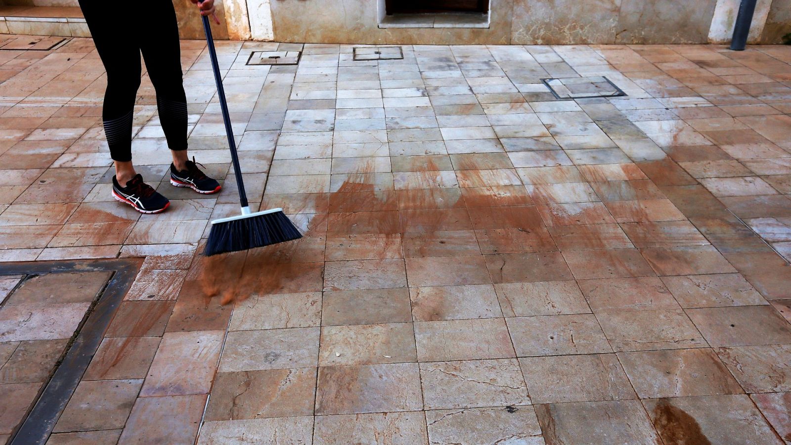 Una mujer limpia el barro depositado por la precipitación de polvo sahariano en el Levante