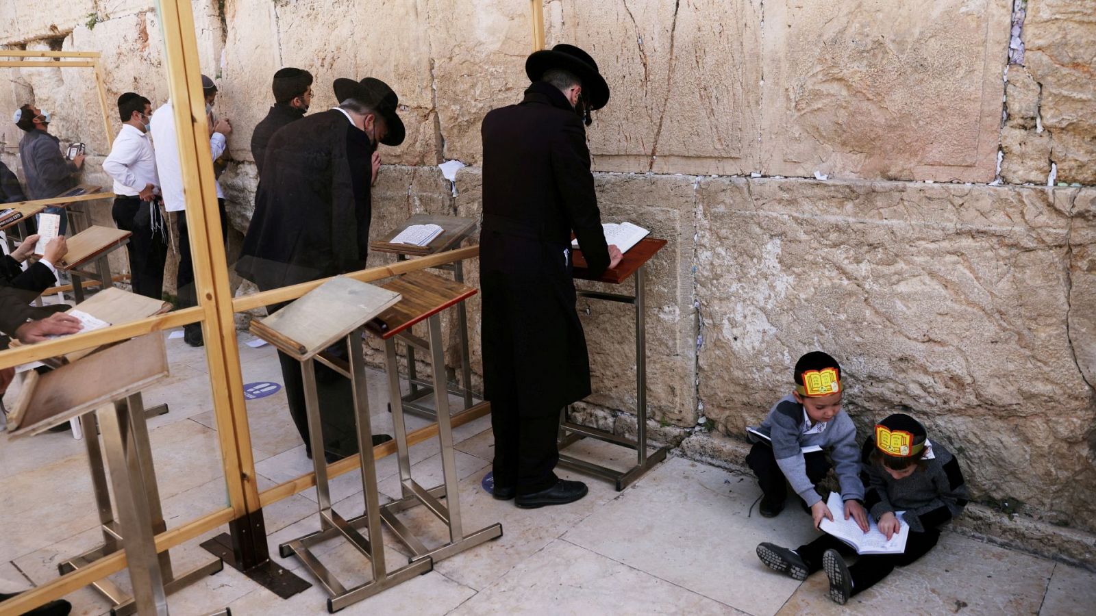 Niños judíos ultraortodoxos juegan mientras varios hombres rezan frente al Muro de las Lamentaciones de Jerusalén