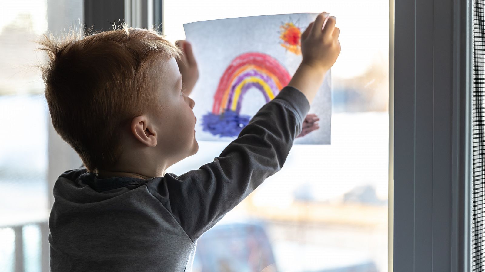 Un niño cuelga un dibujo con un arco iris durante el confinamiento domiciliario.