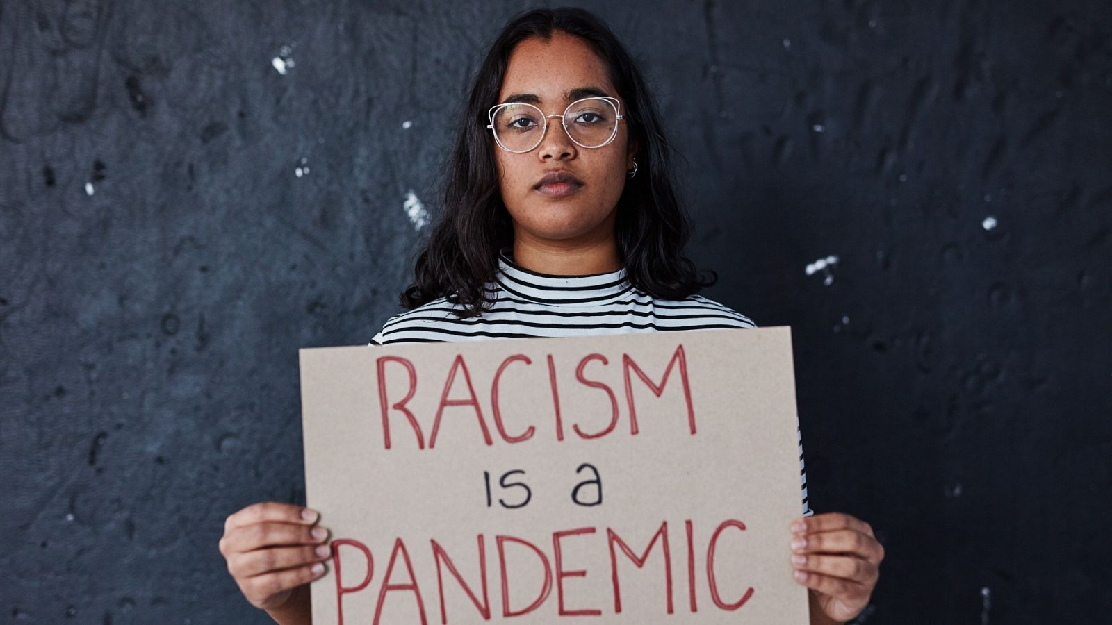 Una joven sostiene un cartel que denuncia "El racismo es una pandemia"