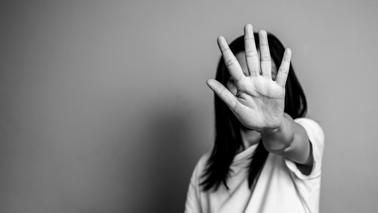 Una mujer se tapa la cara y muestra su mano, en rechazo a la violencia machista