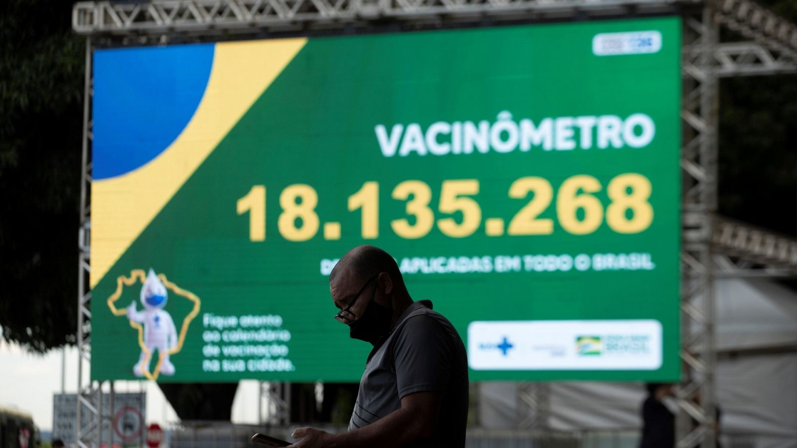 Un hombre observa su teléfono frente al "vacunómetro", un tablero digital donde se registra el número de personas vacunadas en el país, este martes en Brasilia