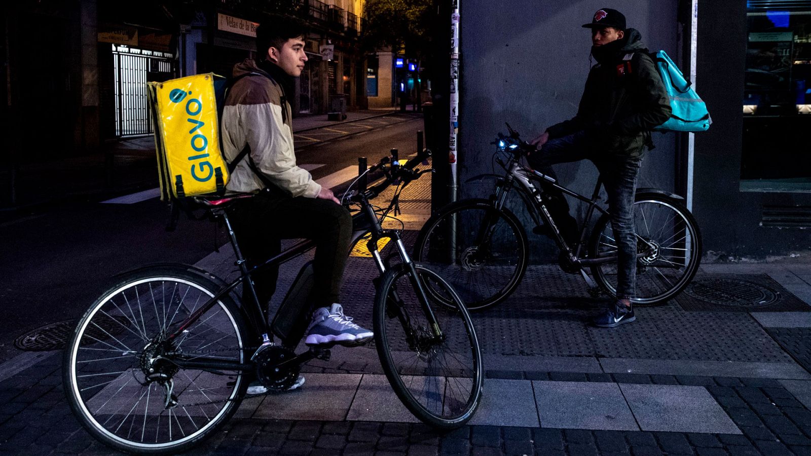 Dos riders esperan un pedido fuera de una comercio en Madrid