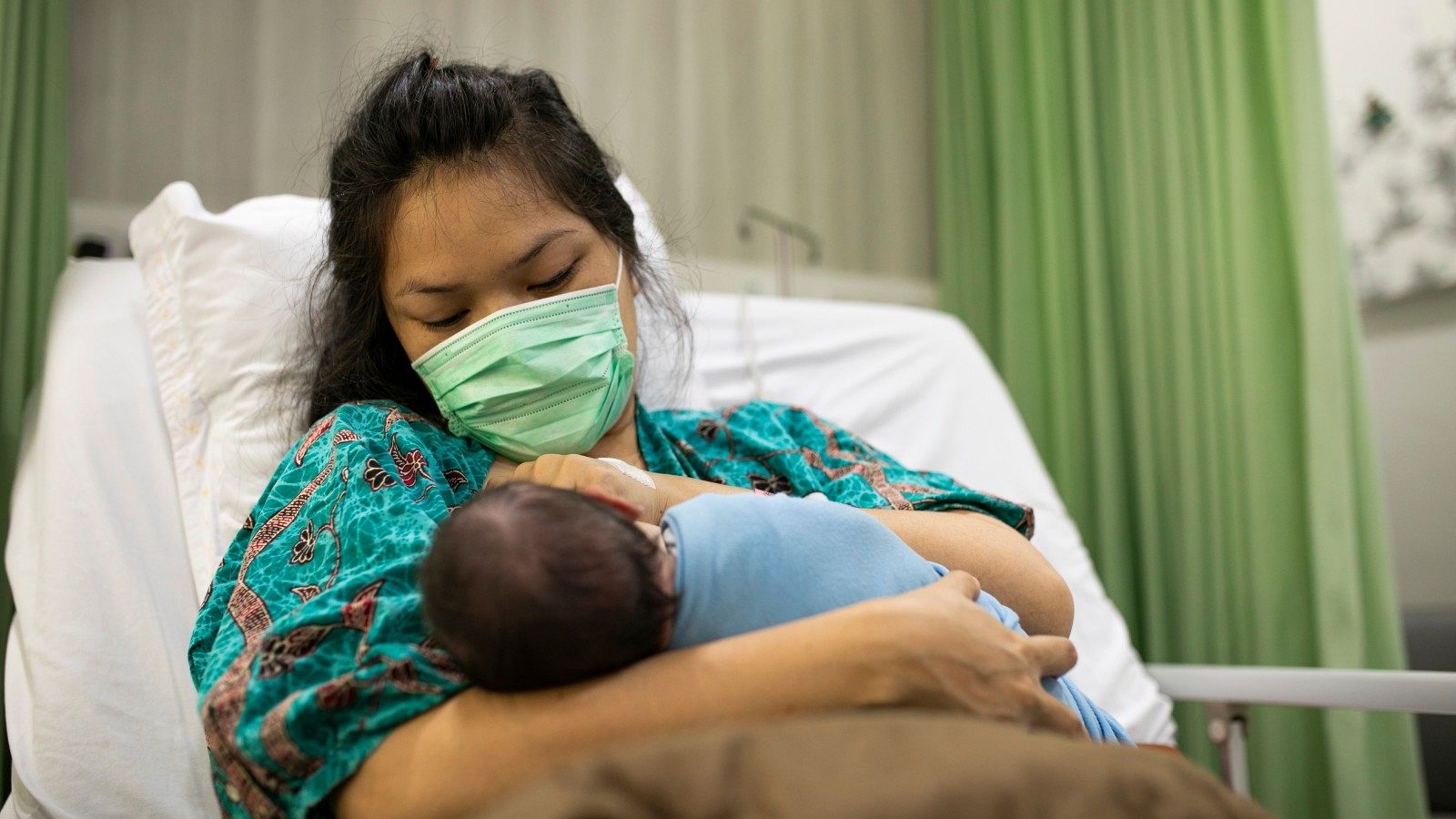 Una madre con mascarilla sostiene a su bebé recién nacido.