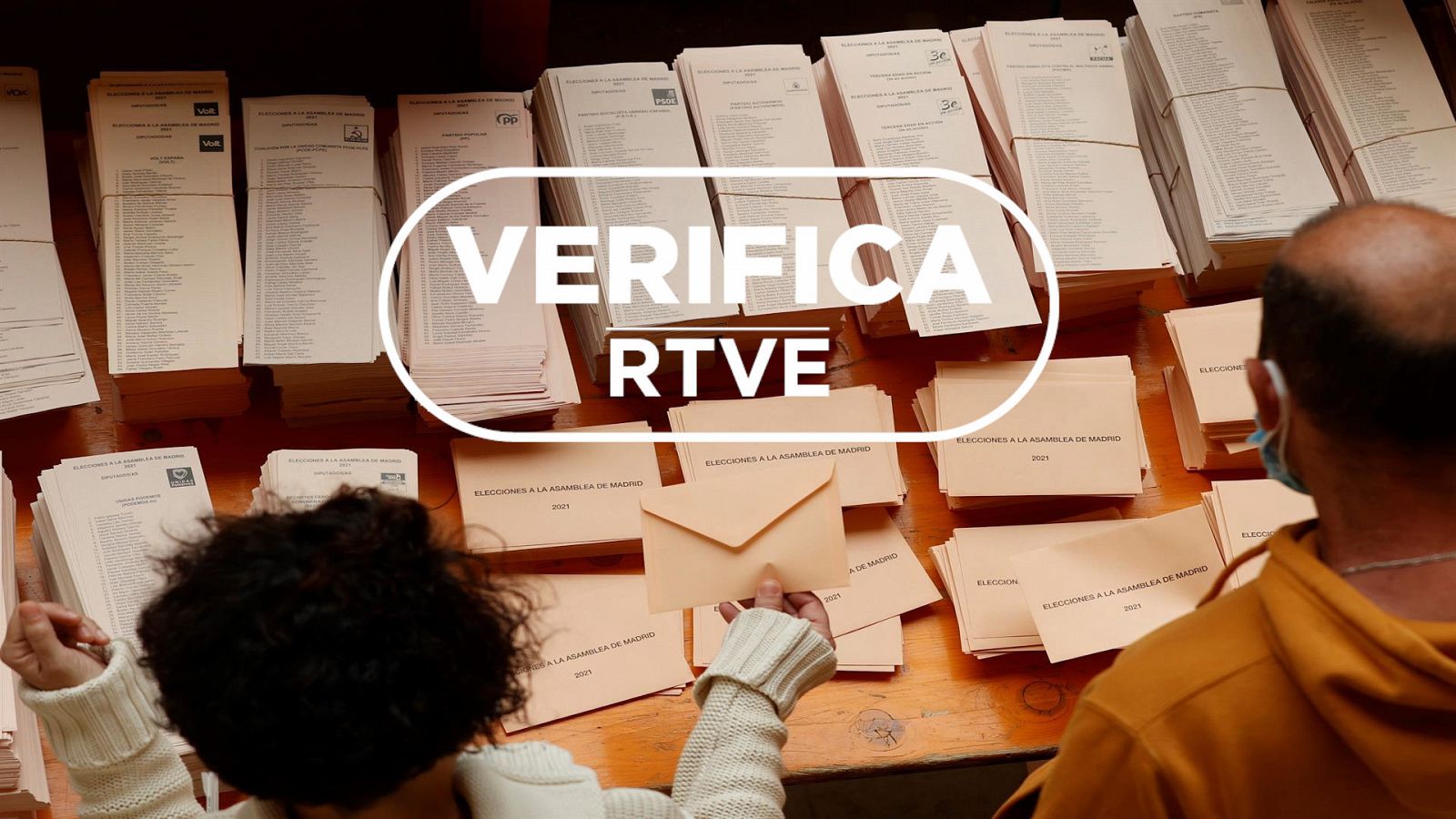 Dos personas eligen la papeleta para votar en las elecciones a la Comunidad de Madrid con el sello de VerificaRTVE.