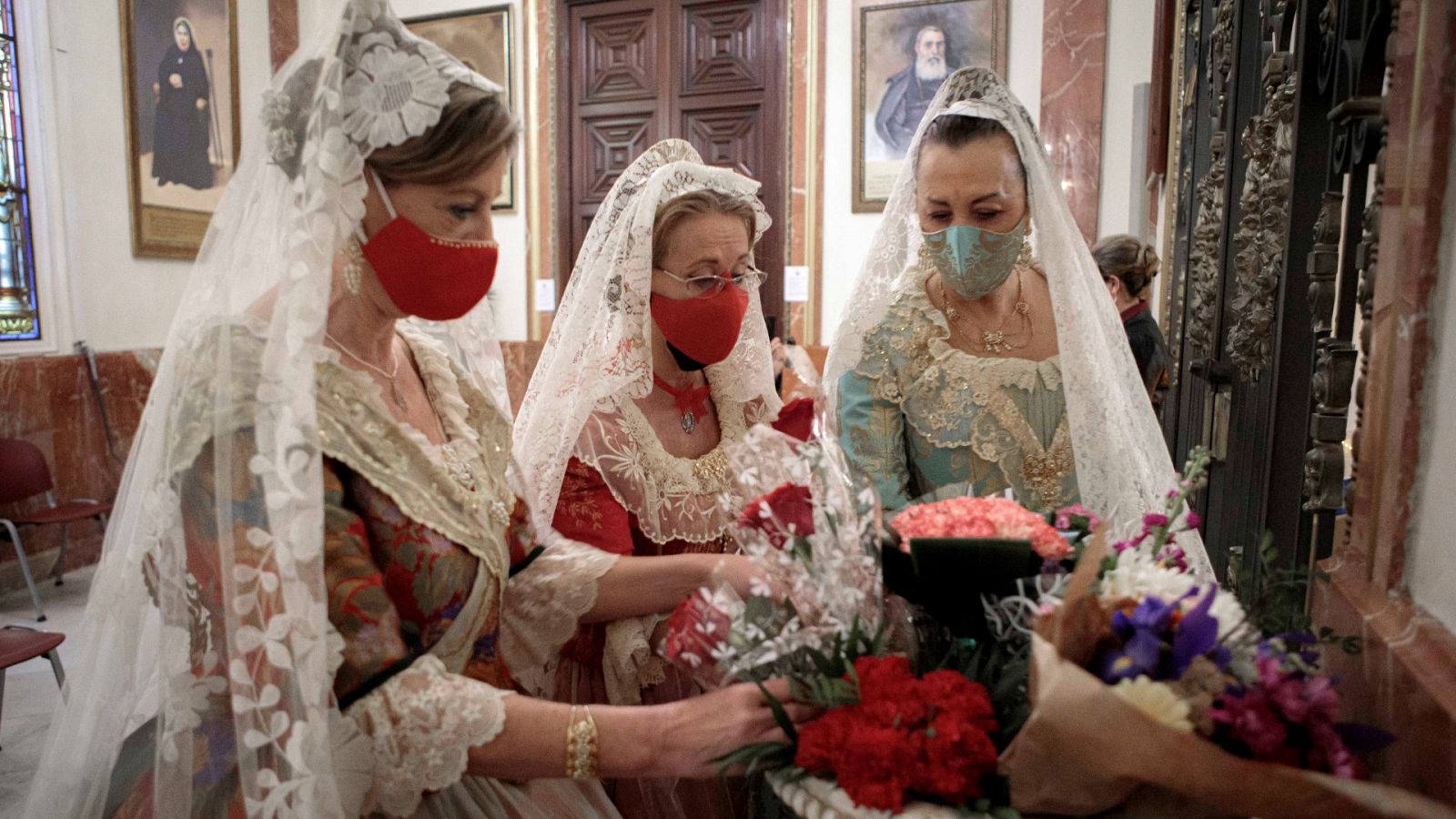Varias mujeres con vestido de fallera realizan una ofrenda floral a la virgen de los Desamparados