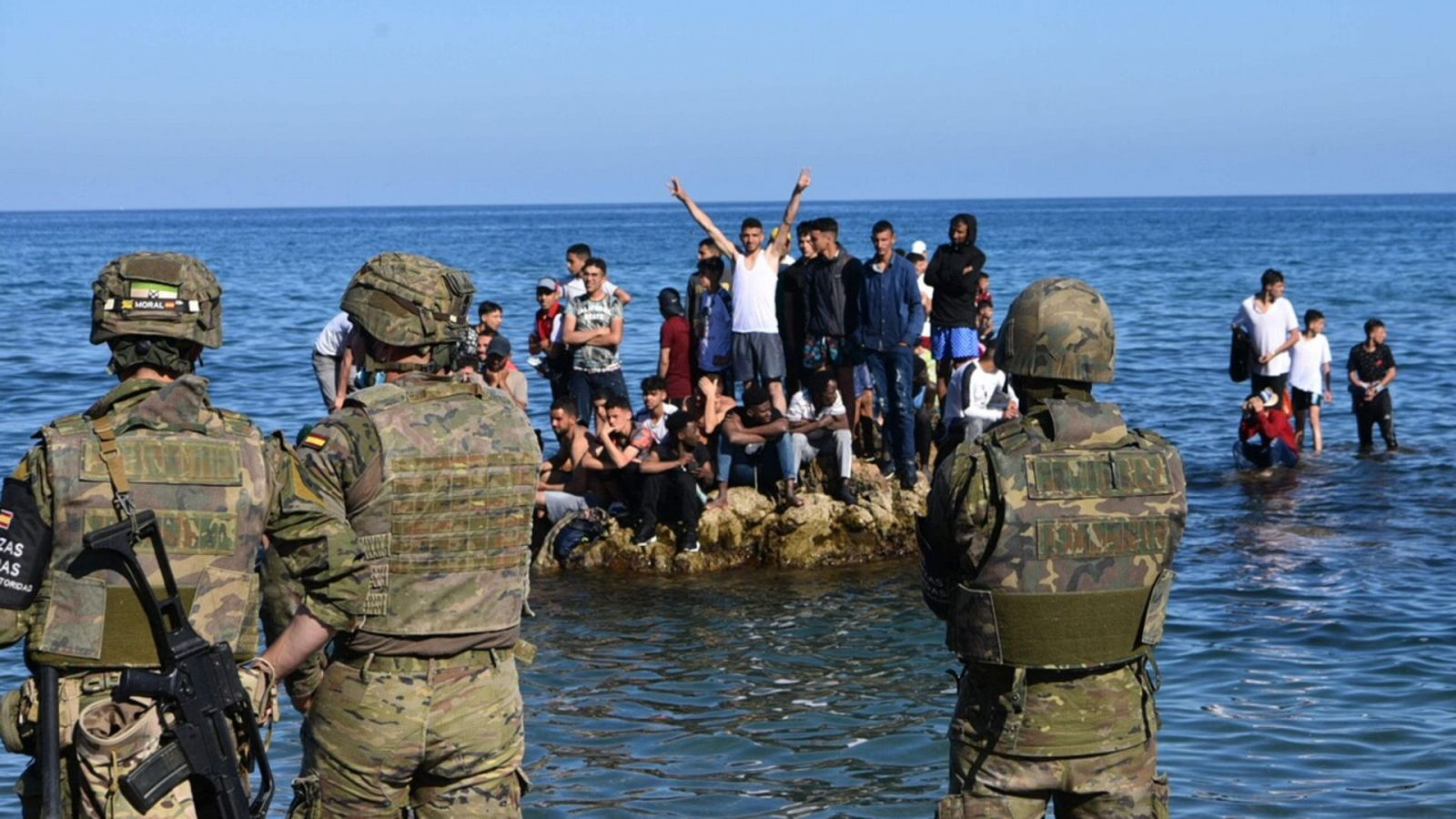 Soldados españoles montan guardia en la frontera entre España y Ceuta mientras un grupo de personas que han cruzado irregularmente se apiñan en una roca en el mar. Antonio Sempere / AFP