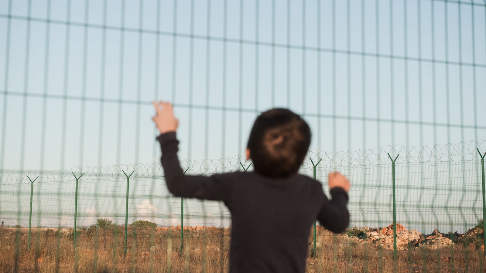 Un niño se agarra a una valla en un campo de inmigrantes