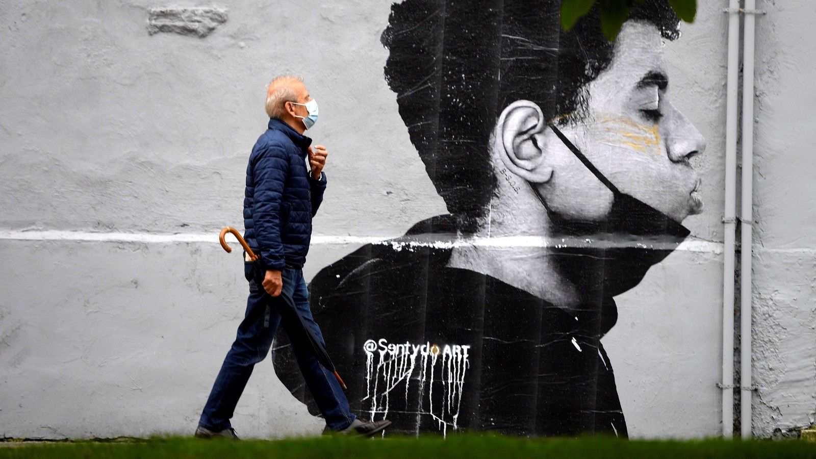 Un hombre con mascarilla camina delante de una obra del artista @Sentydo ART en Oviedo