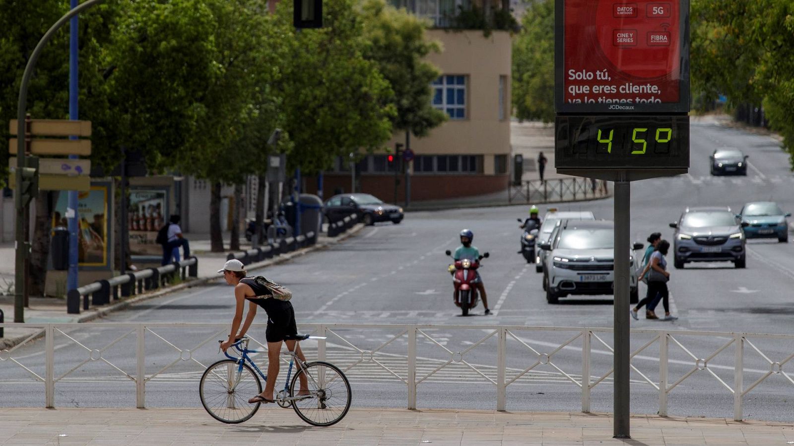Un ciclista pasa junto a un termómetro que marca 45 grados centígrados en Sevilla