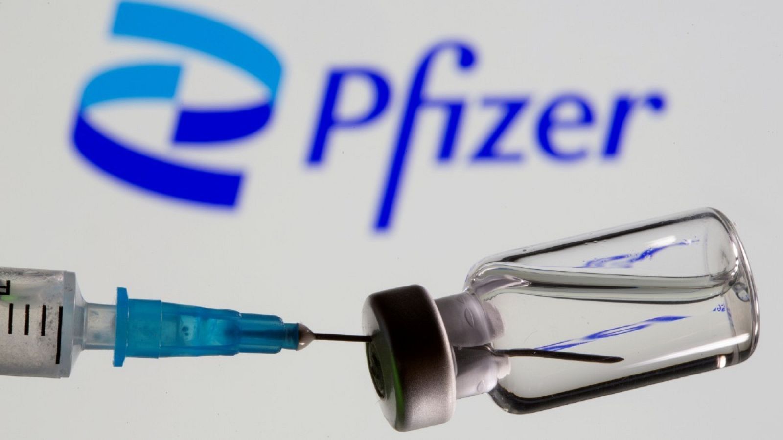 Jeringuilla y vial frente al logotipo de la compañía farmacéutica Pfizer
