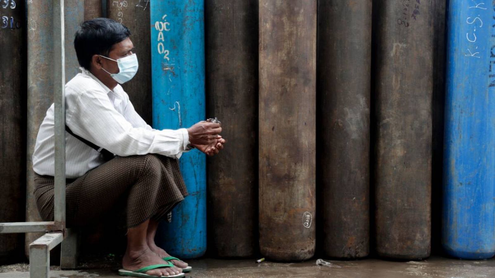 Un hombre de Myanmar con mascarilla se sienta mientras los tanques de oxígeno están alineados para recargarse en una fábrica de oxígeno en Yangon, Myanmar (Birmania). 