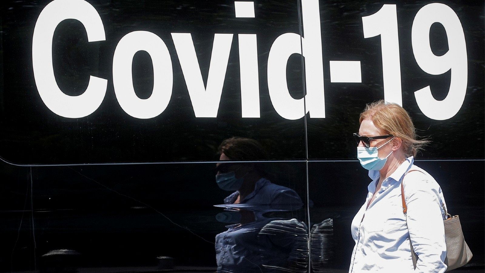 Una mujer con mascarilla pasa junto a una furgoneta que realiza pruebas del coronavirus, en una imagen de archivo