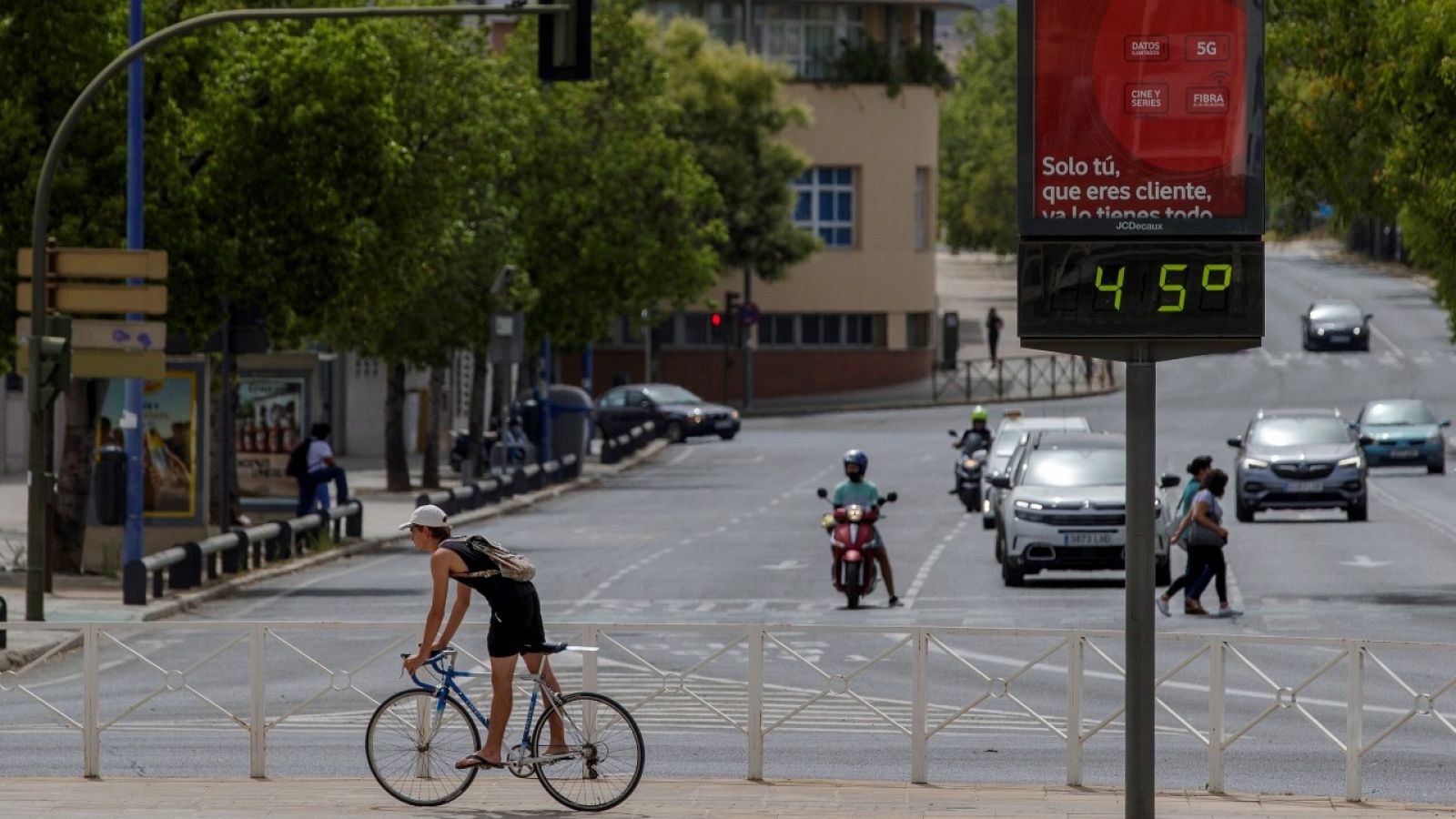 Un ciclista pasa junto a un termómetro que marca 45 grados en Sevilla, en julio