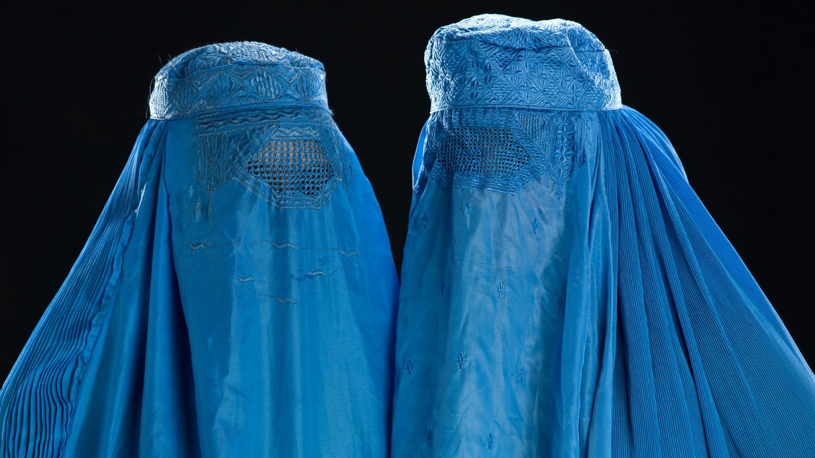 Dos mujeres con burka azul y fondo negro.