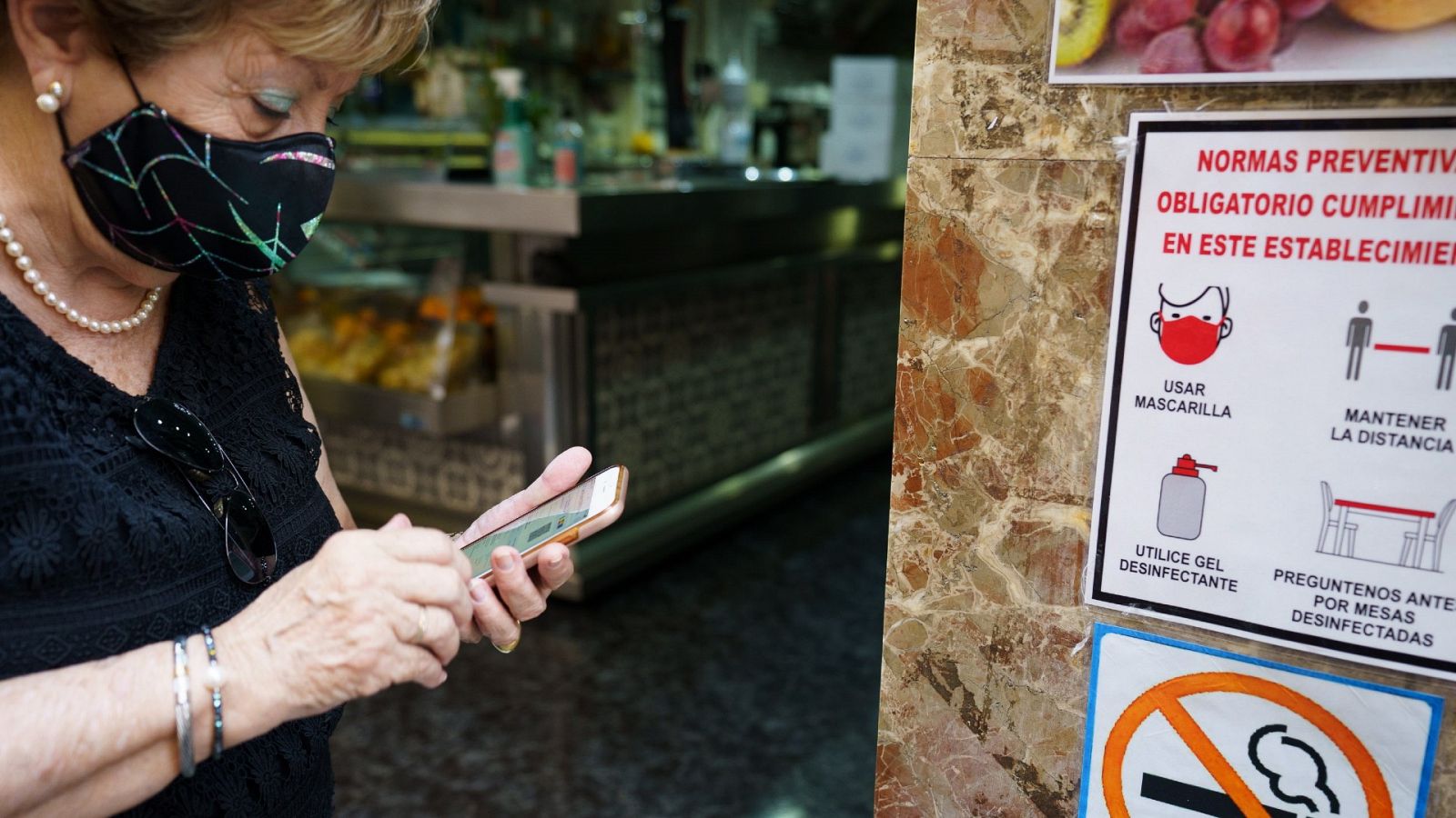 Una mujer busca en su móvil su certificado COVID momentos antes de acceder al interior de una cafetería