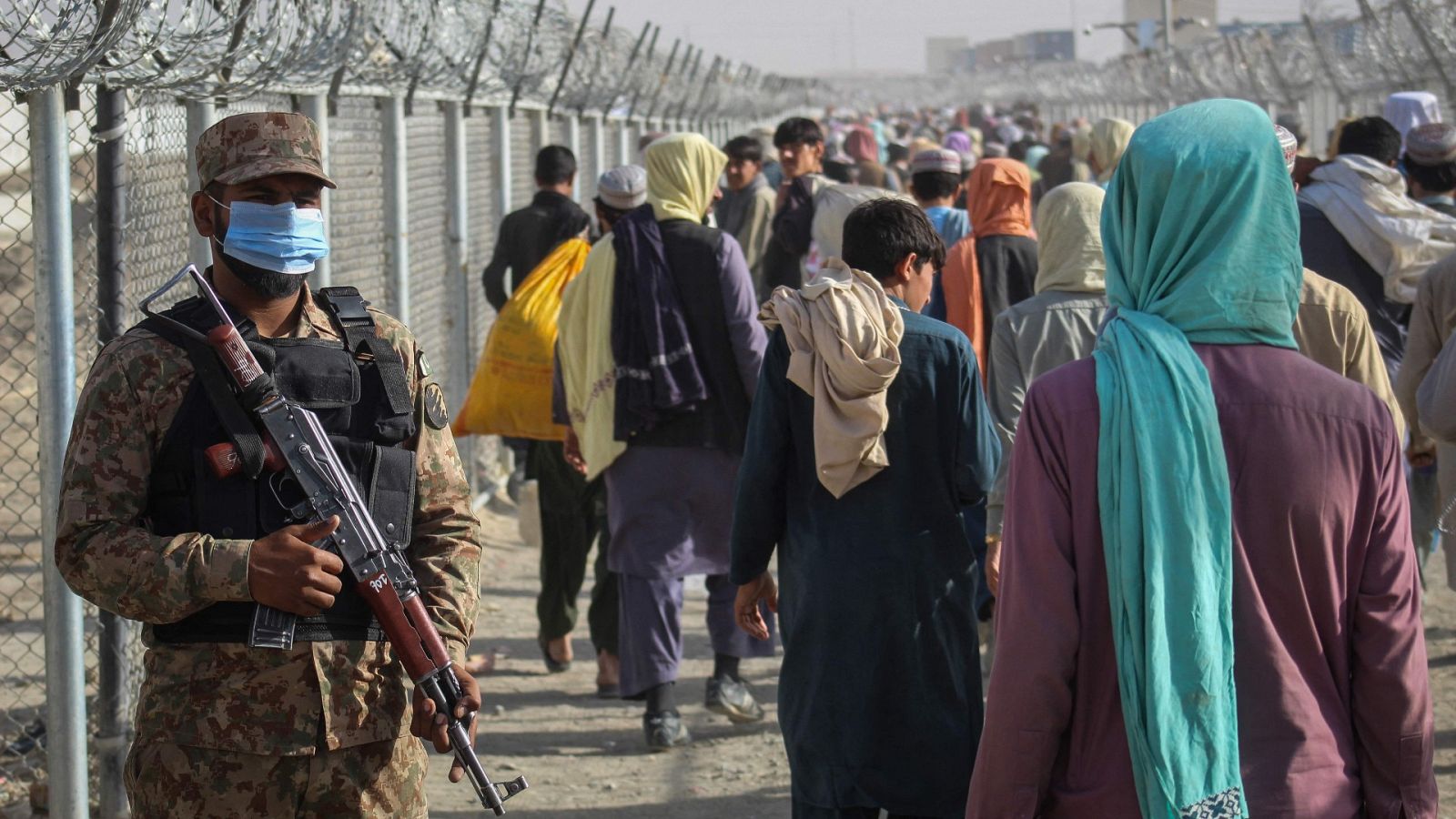 Un soldado paquistaní hace guardia mientras los afganos caminan a lo largo de las vallas después de llegar a Pakistán a través del paso fronterizo entre Pakistán y Afganistán en Chaman el 26 de agosto de 2021