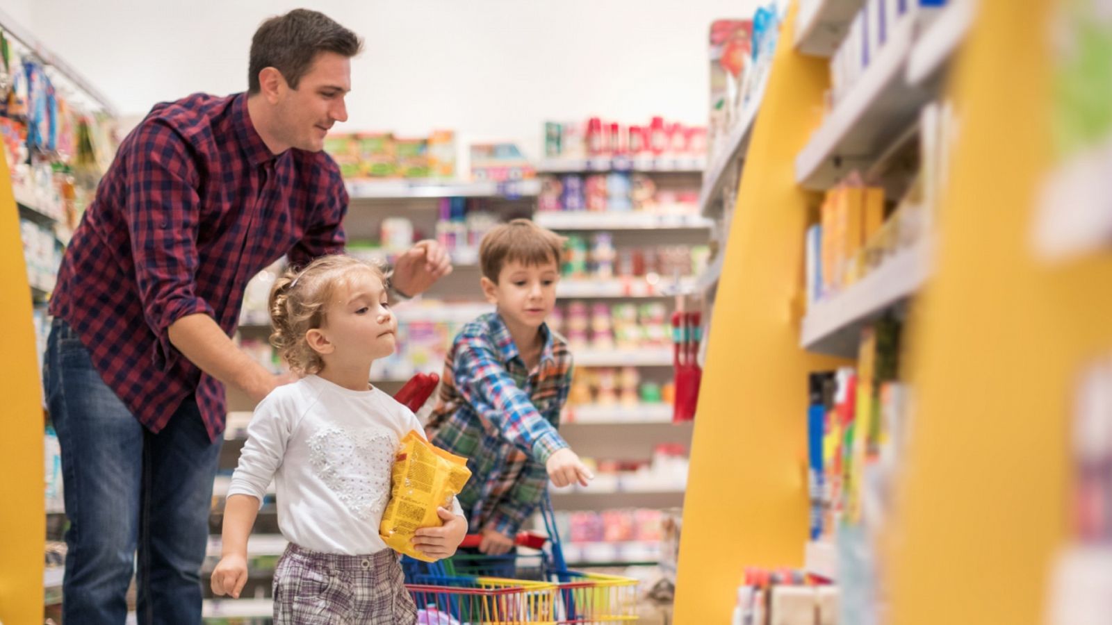 Dos niños acompañan a su padre a hacer la compra en un supermercado.