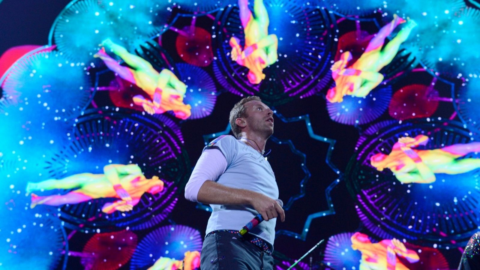 Chris Martin, cantande de Coldplay, cantando sobre un fondo colorido de formas desiguales