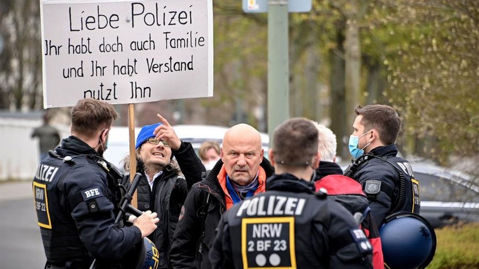 Un manifestante muestra una pancarta que dice 'Querida policía, usted también tiene familia y tiene cerebro, utilícelos', como argumenta con los oficiales de policía durante una manifestación del movimiento 'Querdenker' (pensadores laterales)