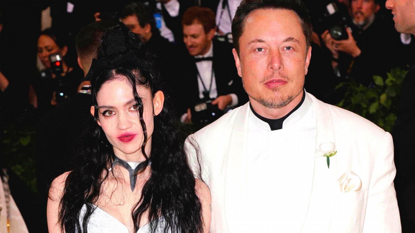 Elon Musk y Grimes en un posado. Él luce de traje blanco y ella, un vestido negro.