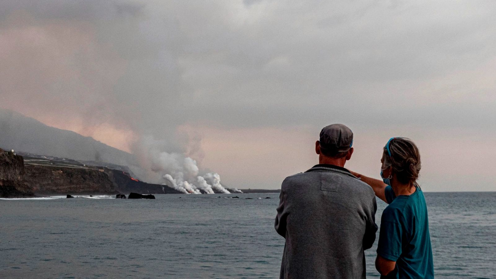 Unos turistas contemplan desde el puerto de Tazacorte la llegada al mar de la colada del volcán Cumbre Vieja