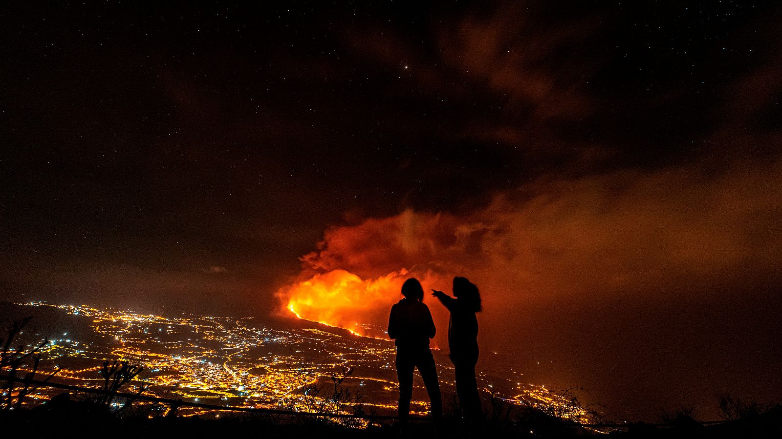 Dos jóvenes contemplan el Valle de Aridane, con la erupción volcánica al fondo.