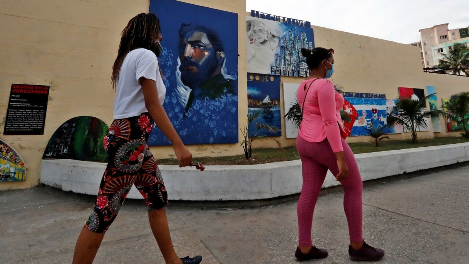 Dos mujeres caminan frente a pinturas en una calle con consignas e imágenes de líderes de la revolución cubana en La Habana (Cuba). EFE/ Ernesto Mastrascusa